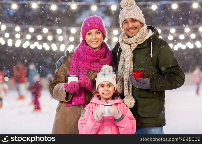 christmas, family and leisure concept - happy mother, father and daughter drinking hot tea at outdoor skating rink in winter. happy family drinking hot tea on skating rink