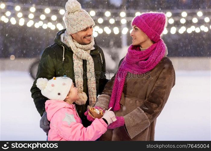 christmas, family and leisure concept - happy mother, father and daughter eating takeaway pancakes at outdoor skating rink in winter. happy family eating pancakes on skating rink