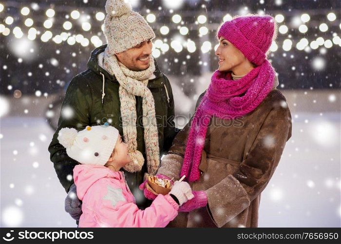 christmas, family and leisure concept - happy mother, father and daughter eating takeaway pancakes at outdoor skating rink in winter over snow. happy family eating pancakes on skating rink
