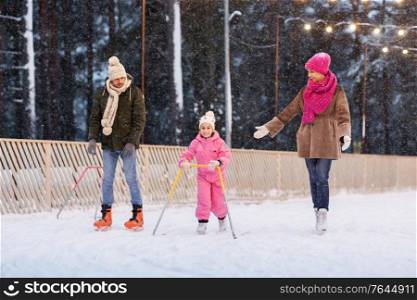 christmas, family and leisure concept - happy mother, father and daughter with support frame at outdoor skating rink in winter. happy family at outdoor skating rink in winter