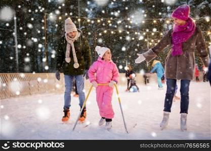 christmas, family and leisure concept - happy mother, father and daughter with support frame at outdoor skating rink in winter over snow. happy family at outdoor skating rink in winter