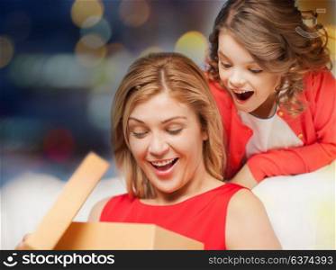 christmas, family and people concept - happy mother and daughter with gift box over festive lights background. happy mother and daughter with gift box