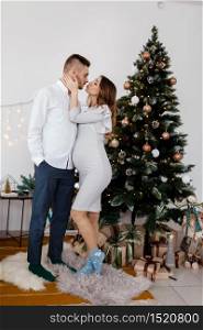 Christmas family photo with christmas tree and ornaments, wooden floor and fireplace. Man and woman are kissing near christmas tree.