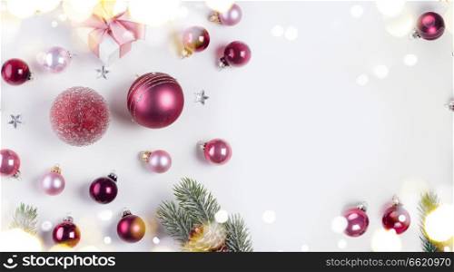 Christmas flat lay border with pink abd violet glass balls, fir tree twigs and gift box, copy space on white desk. Christmas flat lay scene with glass balls