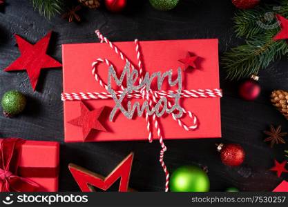 Christmas flat lay scene with red git box, Christmas celebration and gift giving concept, with merry xmas lettering over dark background. Christmas flat lay scene with golden decorations