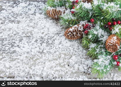 Christmas frame composed of green branches of spruce, pine cones and holly berries on the background of wooden boards, covered with white snow flakes. Flat lay composition for greeting cards, websites, social media, magazines, bloggers, artists etc.