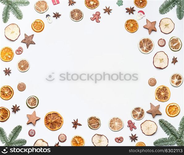 Christmas frame made with fir branches and dried fruits , spices and holiday candies on white desk background. Creative layout for Christmas or winter holidays greeting cards, top view