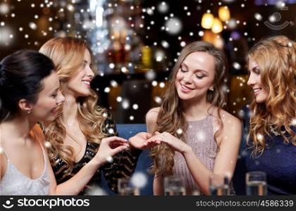 christmas, friends, bachelorette party and winter holidays concept - happy woman showing engagement ring to her friends with champagne glasses at night club over snow