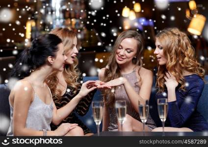 christmas, friends, bachelorette party and winter holidays concept - happy woman showing engagement ring to her friends with champagne glasses at night club over snow