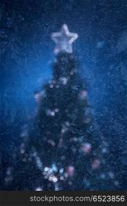 Christmas fur-tree through glass with frosty patterns. Holiday