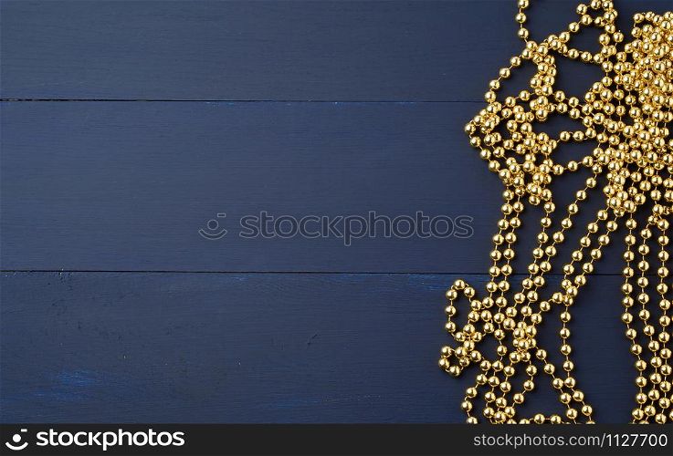 Christmas garland of round golden beads strung on a string, blue wooden background from boards. Golden garland ball christmas shine in beautiful style, copy space