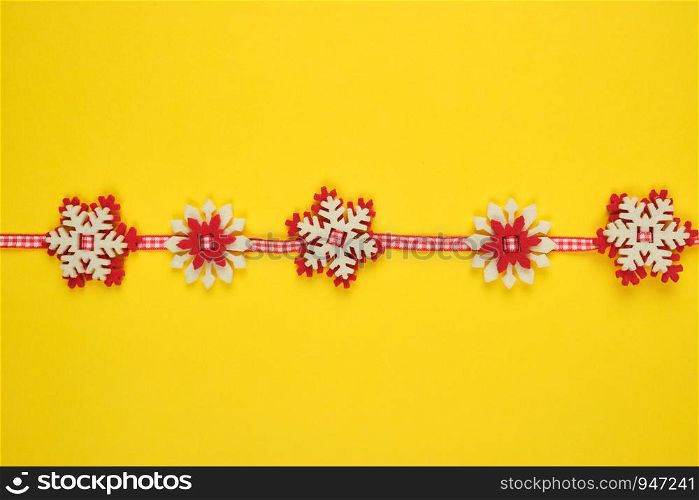 Christmas garland with carved felt snowflakes on a red ribbon, yellow background