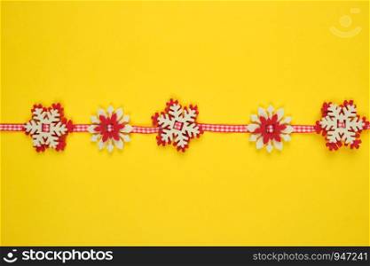 Christmas garland with carved felt snowflakes on a red ribbon, yellow background