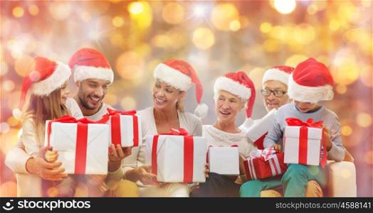 christmas, generation, holidays and people concept - happy family in santa helper hats with gift boxes sitting on couch over lights background