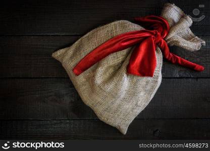 Christmas gift bag with red ribbon on wooden background