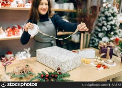 Christmas gift box wrapping and decoration process. Woman wraps present on the table, decor procedure, festive package. Christmas gift box wrapping and decoration process