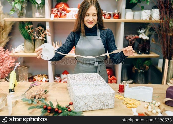 Christmas gift box wrapping and decoration process. Woman wraps present on the table, decor procedure, festive package