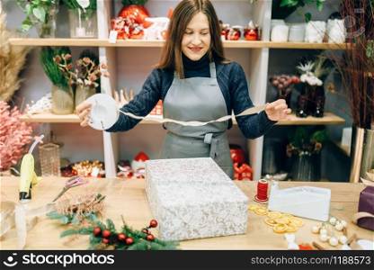 Christmas gift box wrapping and decoration process. Woman wraps present on the table, decor procedure, festive package