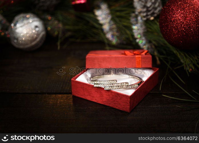 Christmas gift in red box with red ribbon on wooden background, surrounded by a Christmas wreath