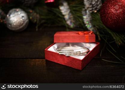 Christmas gift in red box with red ribbon on wooden background, surrounded by a Christmas wreath