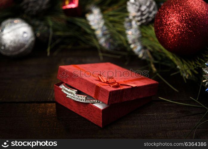 Christmas gift in red box with red ribbon on wooden background, surrounded by a Christmas wreath