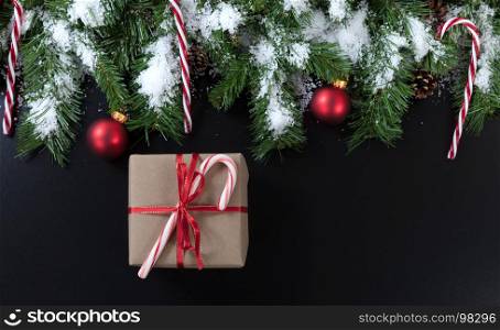 Christmas gift with snowy evergreen tree branches, candy canes and red ornaments on black background