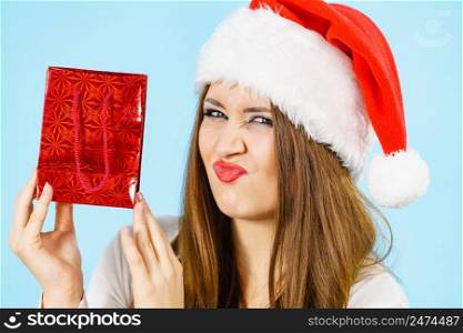 Christmas gifts. Funny woman wearing santa claus hat holding present red gift bag, on blue. Funny Christmas woman holds red gift bag