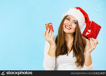 Christmas gifts. Happy woman wearing santa claus hat holding present red bag and small gift box with jewelery, on blue. Happy Christmas woman holds red gift box