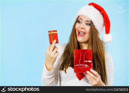 Christmas gifts. Happy woman wearing santa claus hat holding present red bag and small gift box with jewelery, on blue. Happy Christmas woman holds red gift box