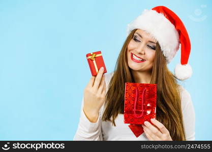 Christmas gifts. Happy woman wearing santa claus hat holding present red bag and small gift box with jewelery, on blue. Happy Christmas woman holds red gift box