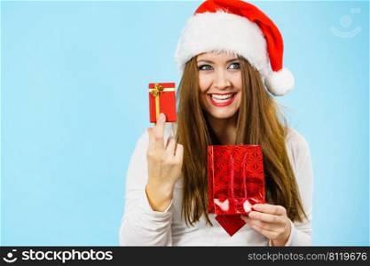 Christmas gifts. Happy woman wearing santa claus hat holding present red bag and small gift box with jewelery, on blue. Happy Christmas woman holds red gift box