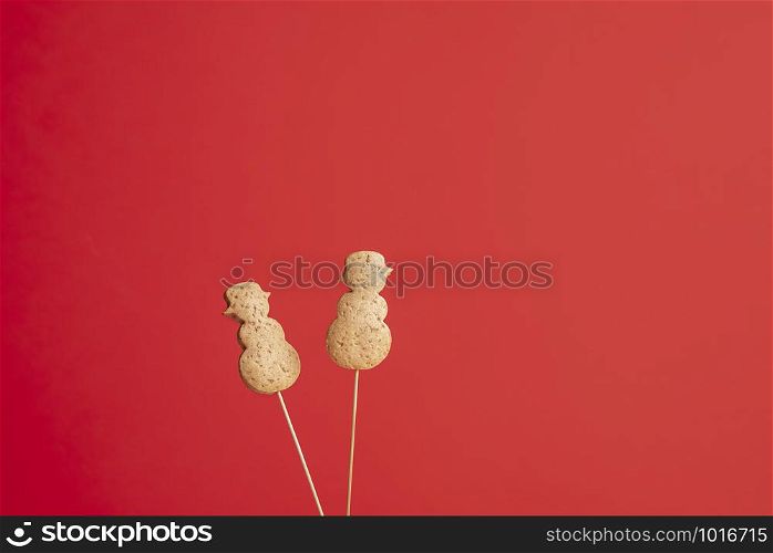 Christmas gingerbread cookies in snowman shape on a stick, on a red background. Xmas famous dessert. Christmas traditional cookies on skewers.