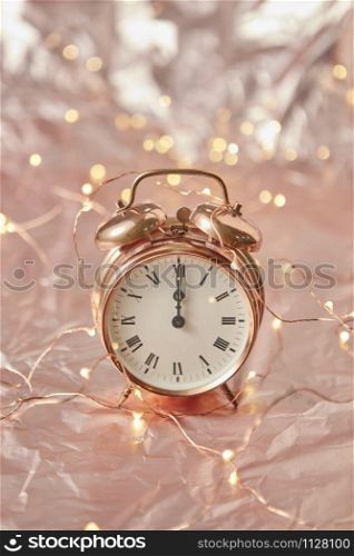 Christmas golden alarm clock on a shiny golden abstract background with copy space. The time is exact midnight. Greeting card.. Holiday card with cooper alarmclock and string of lights.