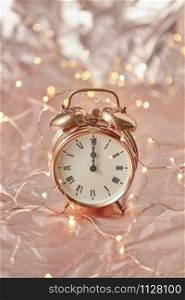 Christmas golden alarm clock on a shiny golden abstract background with copy space. The time is exact midnight. Greeting card.. Holiday card with cooper alarmclock and string of lights.