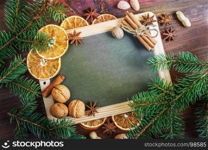 Christmas greeting card: blank chalkboard surrounded by green fir branches, nuts, oranges and spices