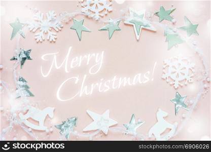 Christmas greeting card composed of white christmas decoration: snowflakes, stars, Christmas trees and toy; rocking horse on pink background with inscription Merry Christmas! Flat lay composition for greeting card, websites, social media, magazines, bloggers, artists etc.