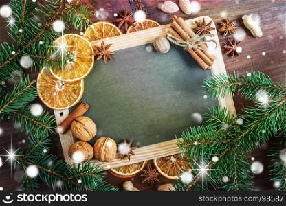 Christmas greeting card: empty chalkboard surrounded by green fir branches, nuts, oranges and spices, with space for text