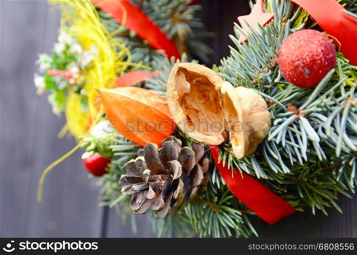 Christmas handmade decorative wreath with small ornaments and red ribbons on wooden background.