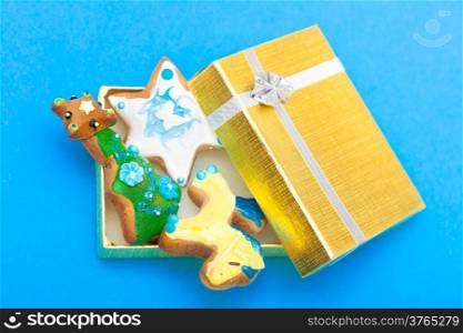 Christmas handmade gingerbread cakes with icing and decoration sweet dessert in golden gift box with silver ribbon on blue background. Holiday concept.