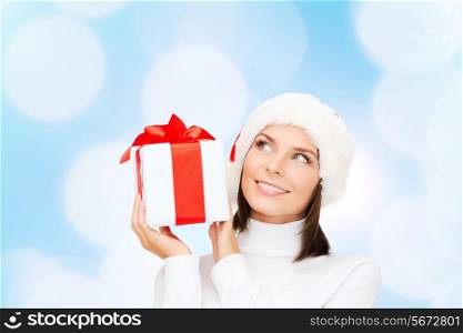 christmas, happiness, holidays and people concept - smiling woman in santa helper hat with gift box over blue lights background