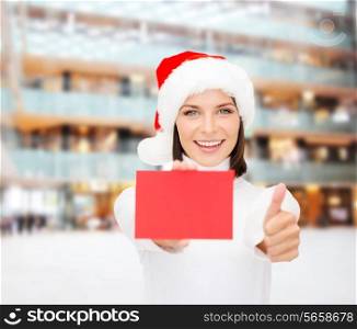 christmas, holdays, people, advertisement and sale concept - happy woman in santa helper hat with blank red card showing thumbs up gesture over shopping center background