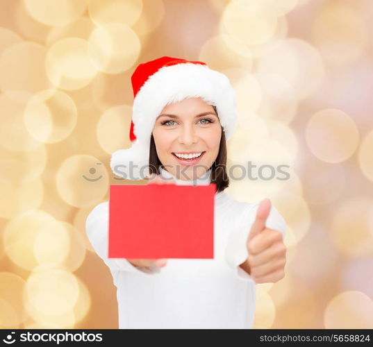 christmas, holdays, people, advertisement and sale concept - happy woman in santa helper hat with blank red card showing thumbs up gesture over beige lights background