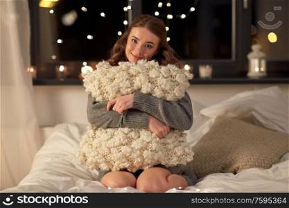 christmas, holiday and people concept - happy young woman with soft pillow in bed at home bedroom at night. happy young woman with soft pillow in bed at home