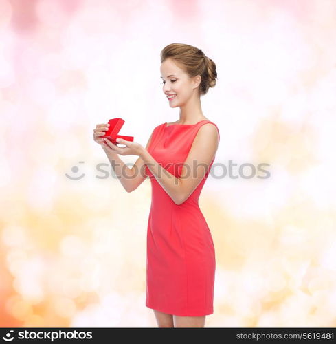 christmas, holiday, valentine&#39;s day and celebration concept - smiling young woman in red dress with gift box