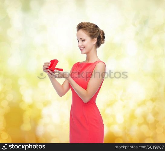 christmas, holiday, valentine&#39;s day and celebration concept - smiling young woman in red dress with gift box