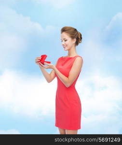 christmas, holiday, valentine&#39;s day and celebration concept - smiling young woman in red dress with gift box