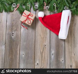 Christmas holiday wooden background with fir branches, Santa cap and gift box forming upper border