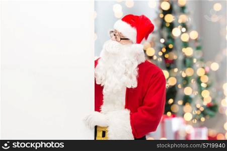 christmas, holidays, advertisement and people concept - man in costume of santa claus with white blank billboard over tree lights background