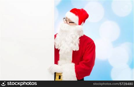 christmas, holidays, advertisement and people concept - man in costume of santa claus with white blank billboard over blue lights background