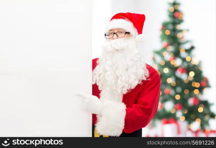 christmas, holidays, advertisement, gesture and people concept - man in costume of santa claus pointing finger to white blank billboard over living room with tree